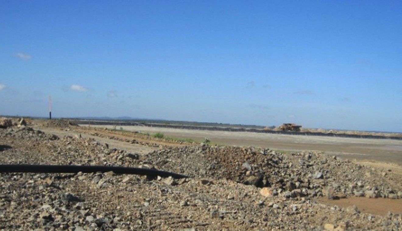 A rockfill embankment under construction with a pipeline laid along it and haul trucks working in the distance