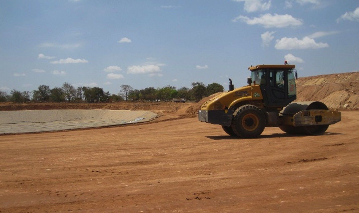 A single-drum roller compacting a prepared earth platform beside a partly lined cell