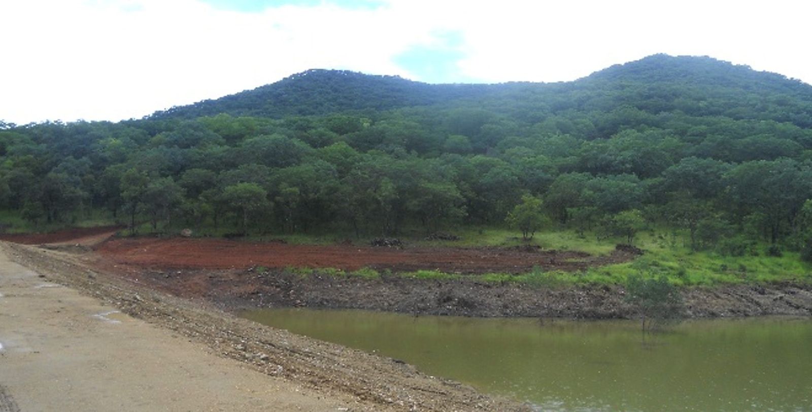A reservoir impounding water at the foot of a forested hill, seen from the crest of its embankment