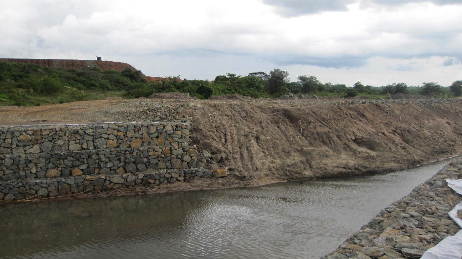 Water flowing past a stone-filled gabion retaining wall and rock-armoured bank